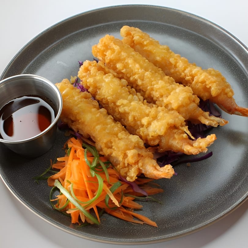 Four crispy fried shrimp tempura with shredded carrots, green onions, and a side of dipping sauce.
