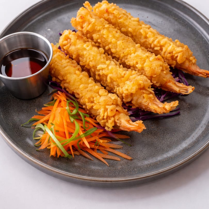 Four crispy fried shrimp tempura with shredded carrots, red cabbage, and a side of dipping sauce.